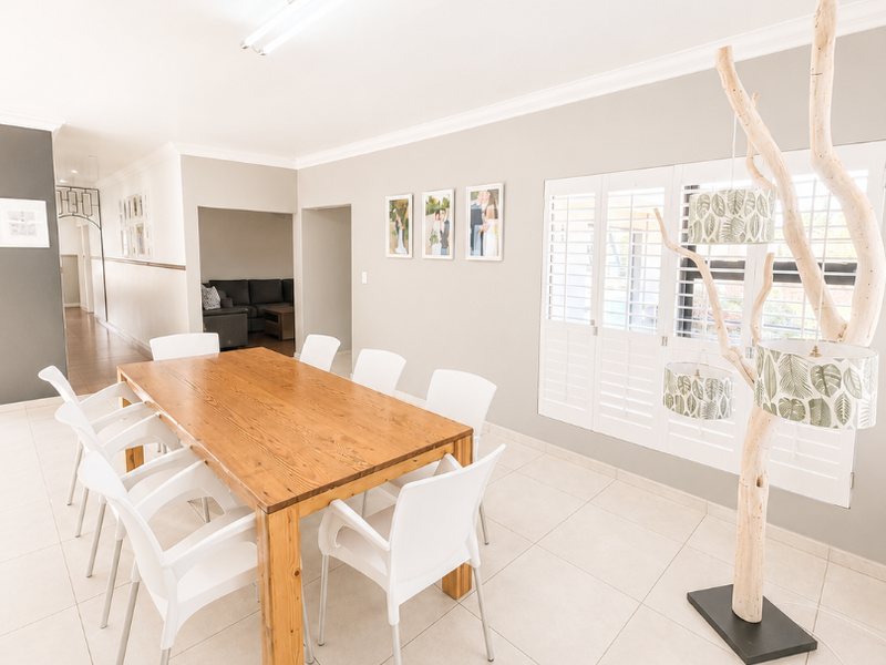 A bright dining room featuring large format floor tiles, plantation shutters, and neutral wall finishes, providing a clean and functional space for family meals.