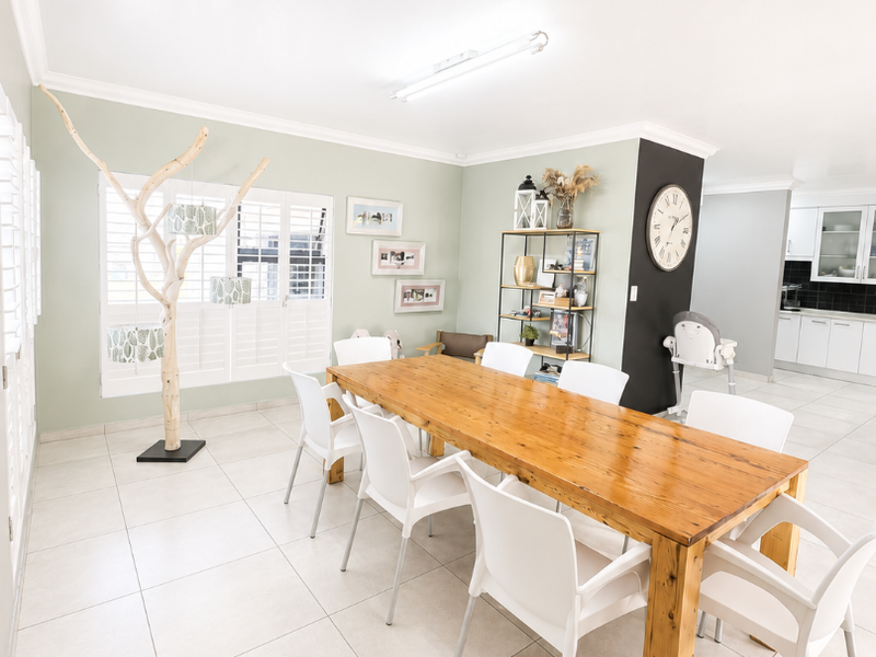 Spacious open-plan dining area featuring light-toned tiled flooring, plantation shutters, and a seamless transition into the adjacent kitchen space.