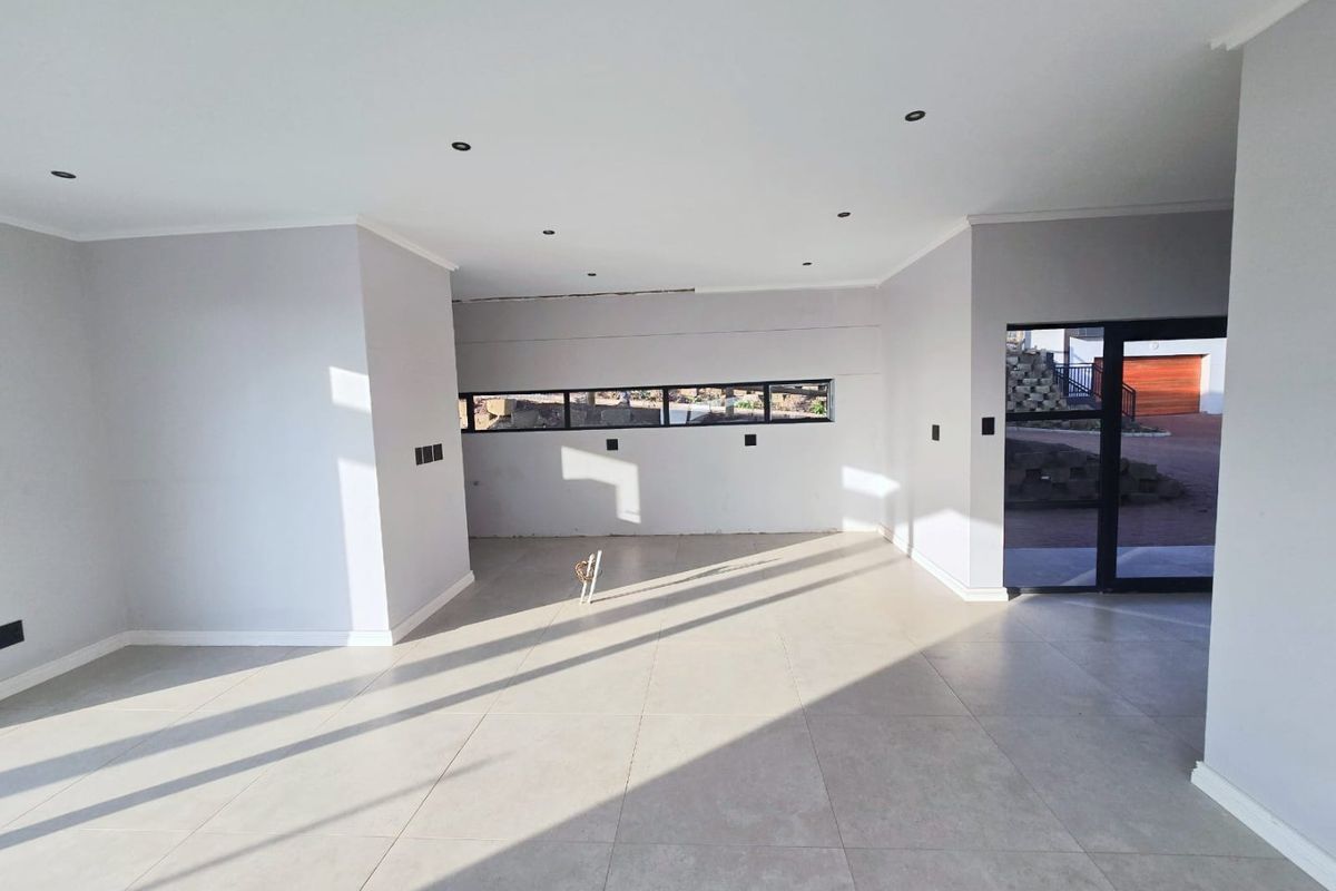 A bright, open-plan living area featuring neutral tiled flooring, recessed downlighting, and modern aluminium-framed windows and doors.