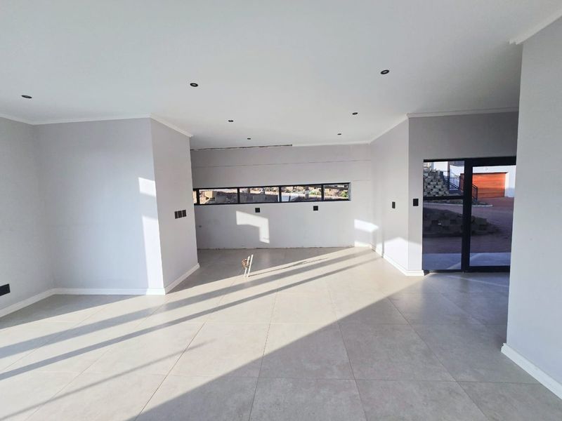 A bright, open-plan living area featuring neutral tiled flooring, recessed downlighting, and modern aluminium-framed windows and doors.