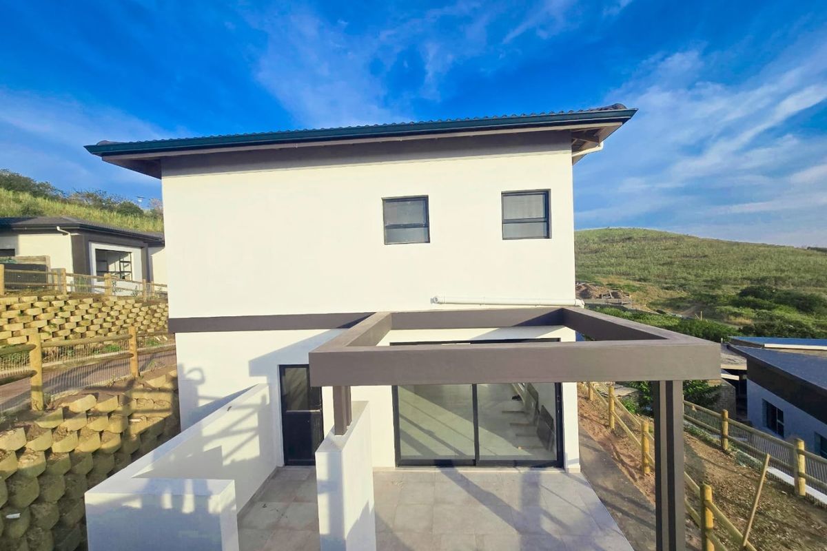 Rear view of a modern two-story house featuring a tiled patio with a pergola, sliding glass doors, and surrounding retaining walls.