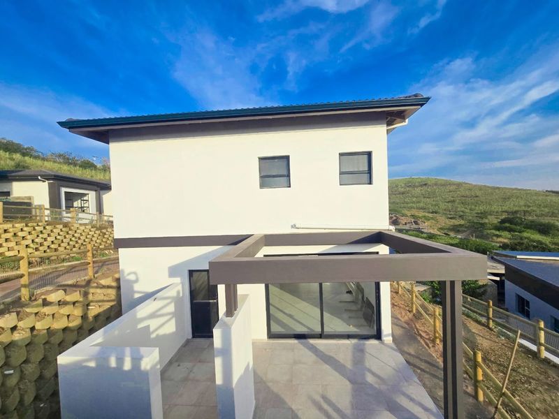Rear view of a modern two-story house featuring a tiled patio with a pergola, sliding glass doors, and surrounding retaining walls.