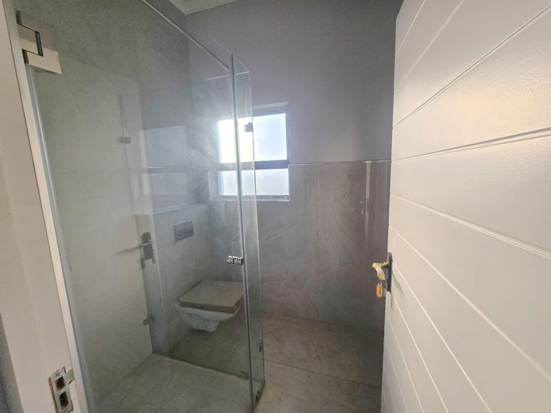 A modern bathroom featuring a glass-enclosed shower and a wall-mounted toilet with neutral tiled finishes.