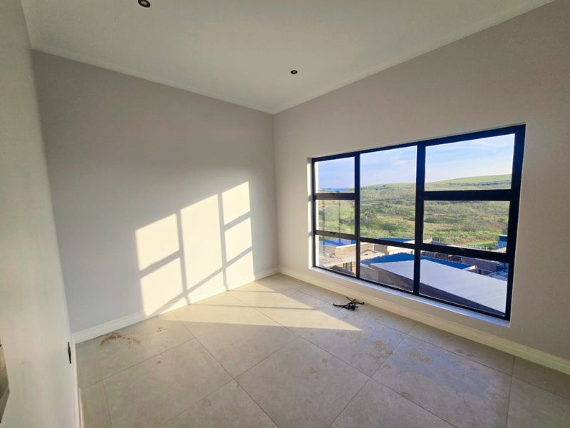 A bright, empty bedroom featuring large black-framed windows with scenic views, neutral walls, and tiled flooring.