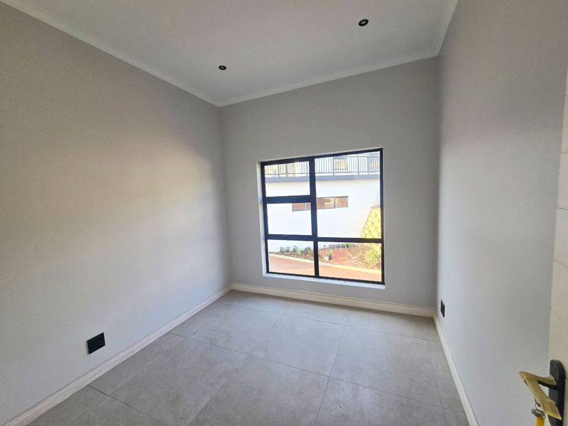A bright, empty bedroom featuring neutral tiled flooring, recessed downlighting, and a modern aluminium-framed window.