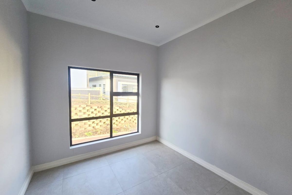 A bright, empty bedroom featuring neutral grey walls, large aluminium-framed windows, and modern tiled flooring with recessed ceiling lighting.