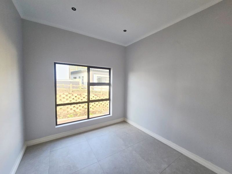 A bright, empty bedroom featuring neutral grey walls, large aluminium-framed windows, and modern tiled flooring with recessed ceiling lighting.