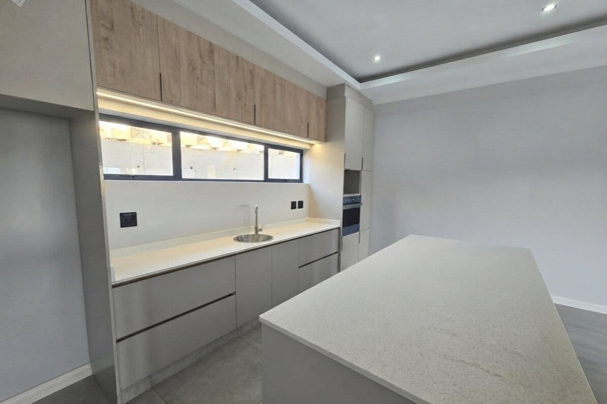 Modern kitchen featuring sleek handleless cabinetry, stone countertops, a central island, built-in oven, and integrated under-cabinet lighting in a neutral color palette.