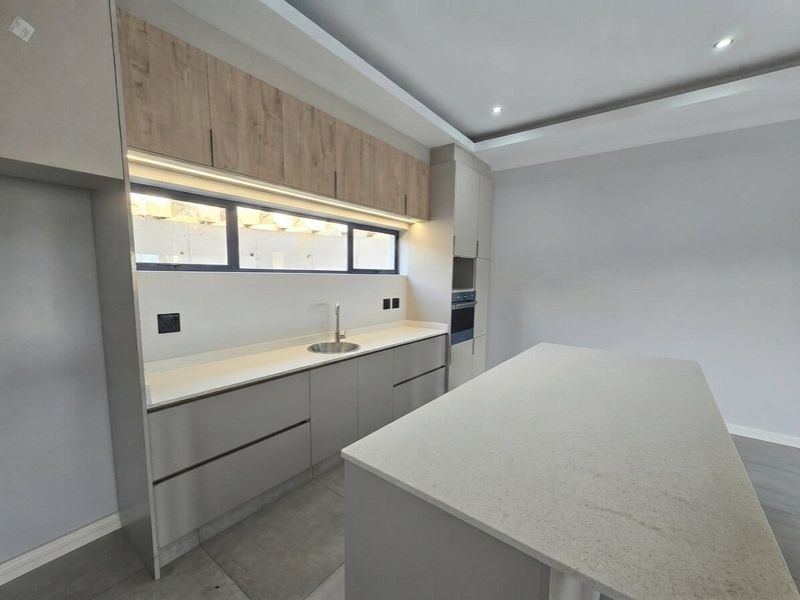 Modern kitchen featuring sleek handleless cabinetry, stone countertops, a central island, built-in oven, and integrated under-cabinet lighting in a neutral color palette.