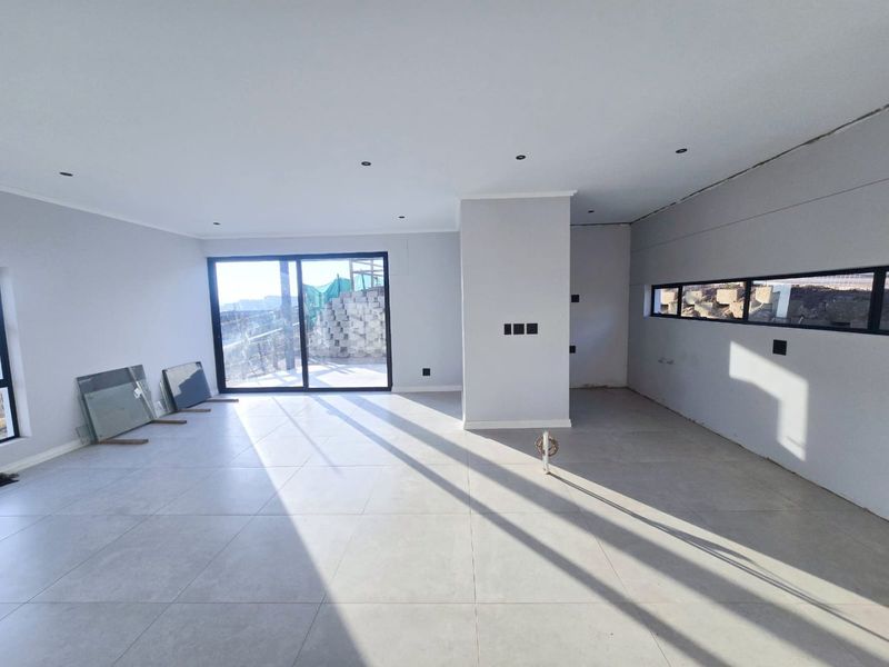 A spacious, open-plan living area featuring large format floor tiles, recessed lighting, and modern sliding glass doors, currently in the final stages of completion.