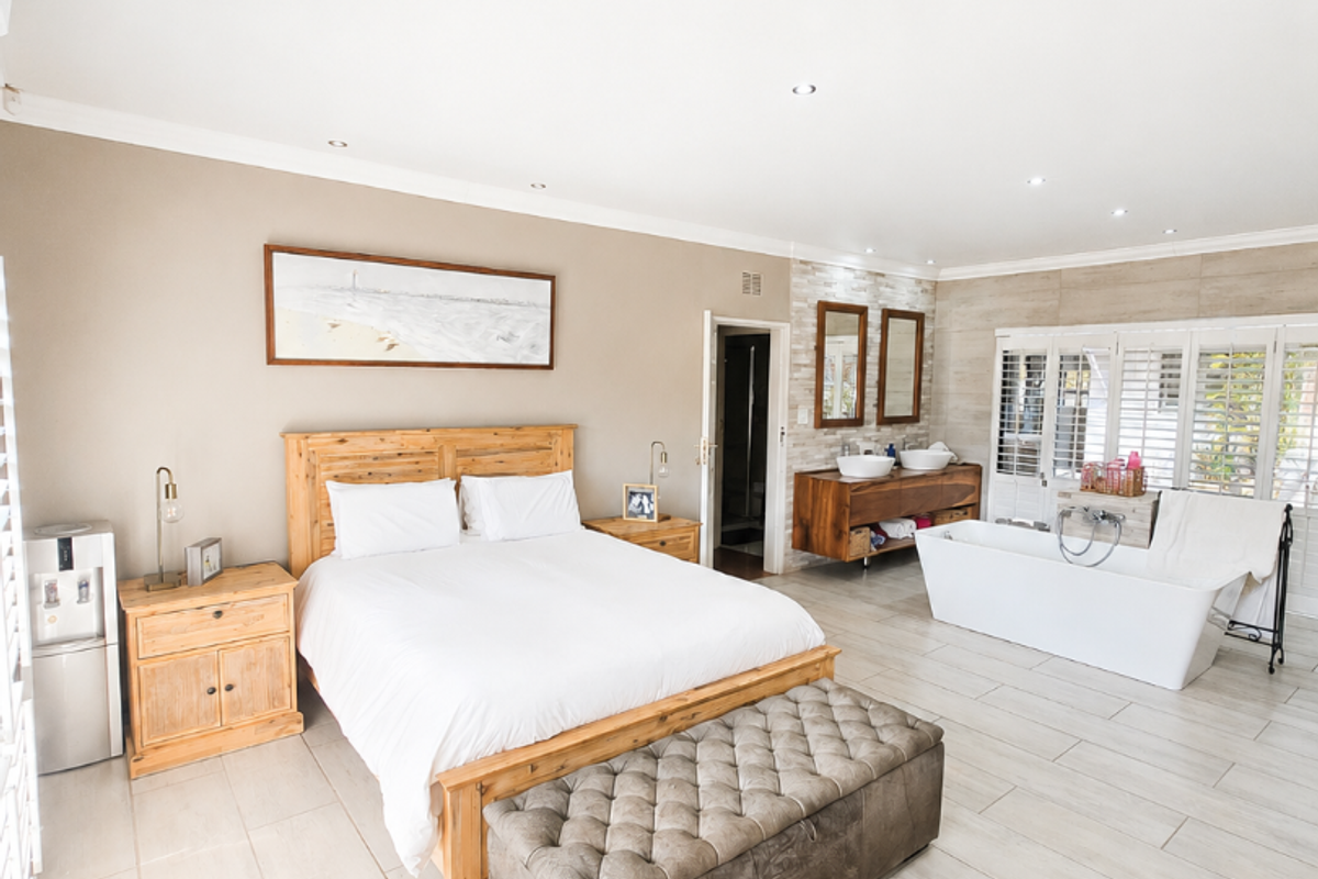 Spacious open-plan bedroom featuring a contemporary ensuite area with a freestanding bathtub, double vanity, and neutral tiled flooring throughout.