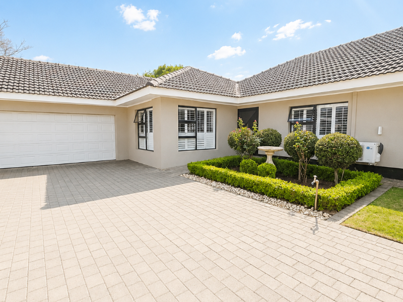 Well-maintained front exterior featuring a spacious paved driveway, double garage, and neat landscaped garden beds under a tiled roof.