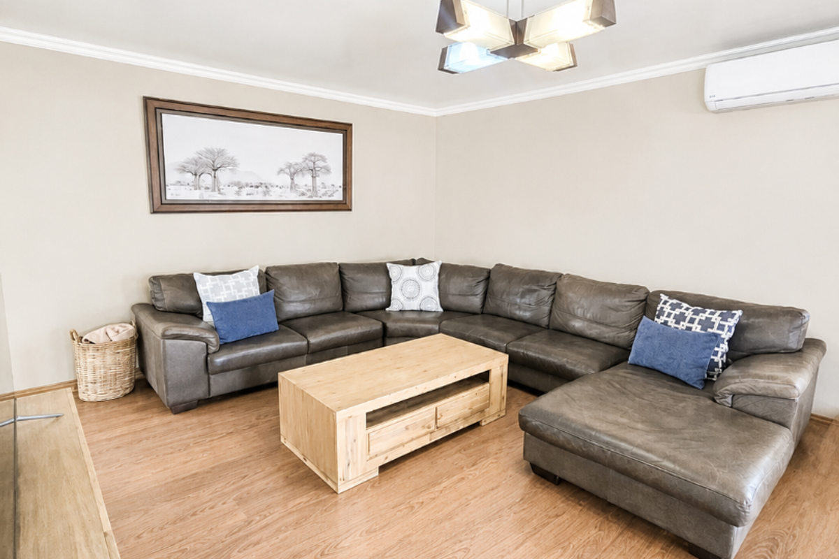 A well-maintained living room featuring laminate flooring, a split-system air conditioner, and a modern ceiling light fixture.