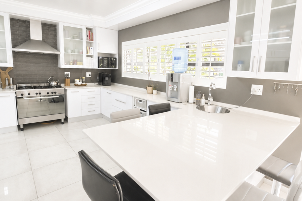 Modern kitchen featuring white cabinetry, stone countertops, a gas stove with stainless steel extractor, and plantation shutters, offering a clean and functional workspace.