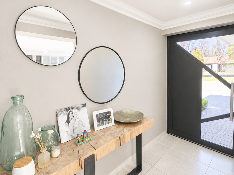 A bright and welcoming entrance hall featuring modern tiled flooring, recessed downlighting, crown molding, and a stylish black framed front door.