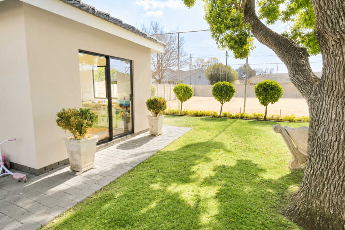 A well-maintained rear garden featuring a paved walkway, mature tree, and a sliding glass door providing access to the home's interior.