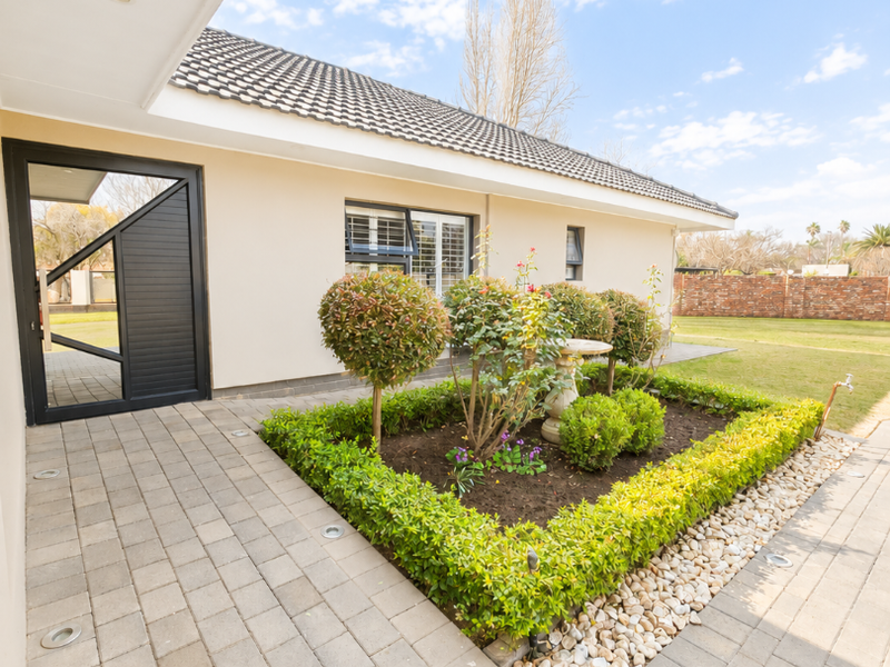A well-maintained paved patio area featuring recessed ground lighting, a landscaped garden bed, and direct access to the home's exterior.