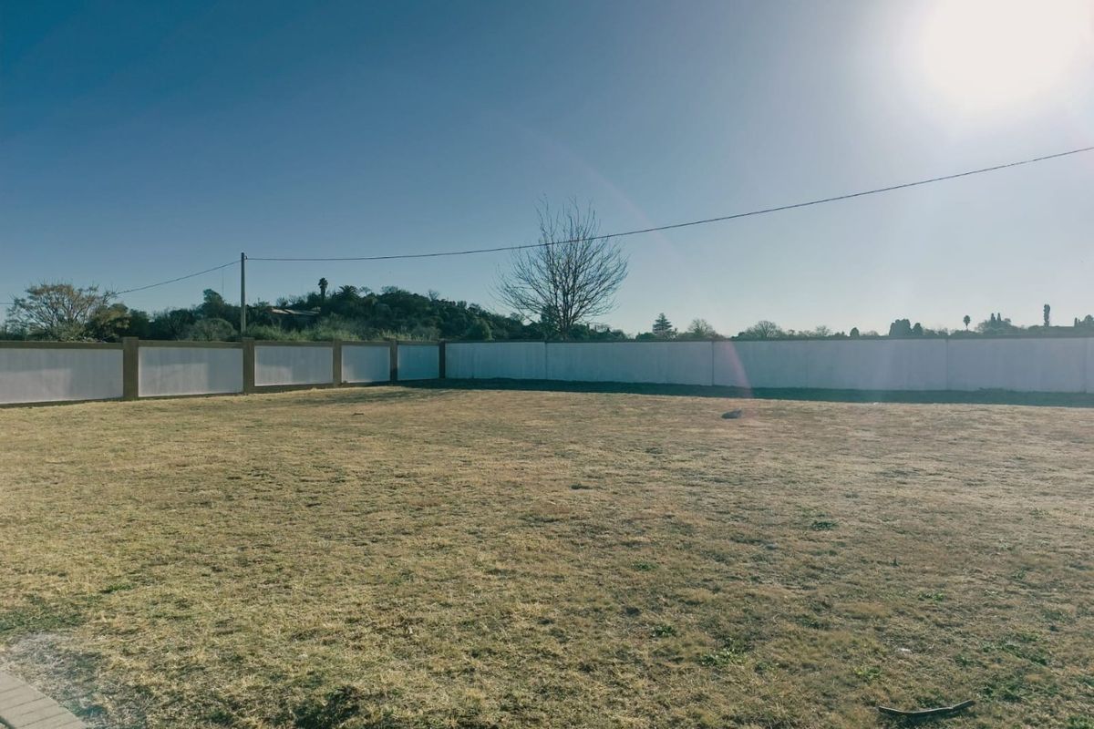 A vacant residential plot featuring a level grassed area enclosed by a perimeter wall with overhead power lines visible.