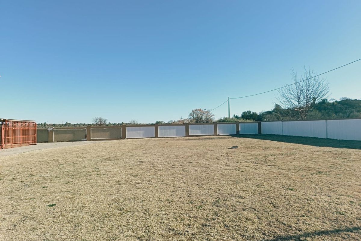 A spacious, level vacant residential plot enclosed by a perimeter wall and metal gate, offering a clear area for future development.