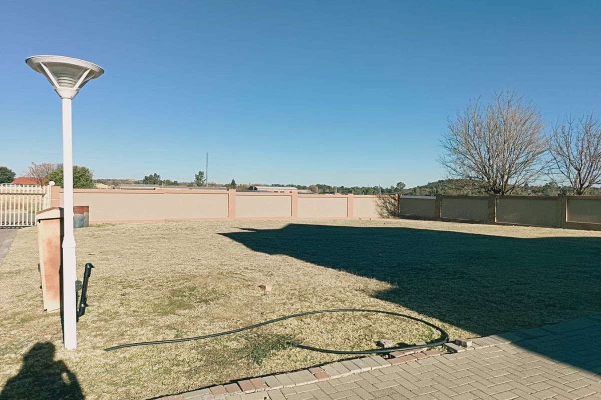 A spacious, level residential garden area featuring a perimeter boundary wall, paved walkway, and established lawn.