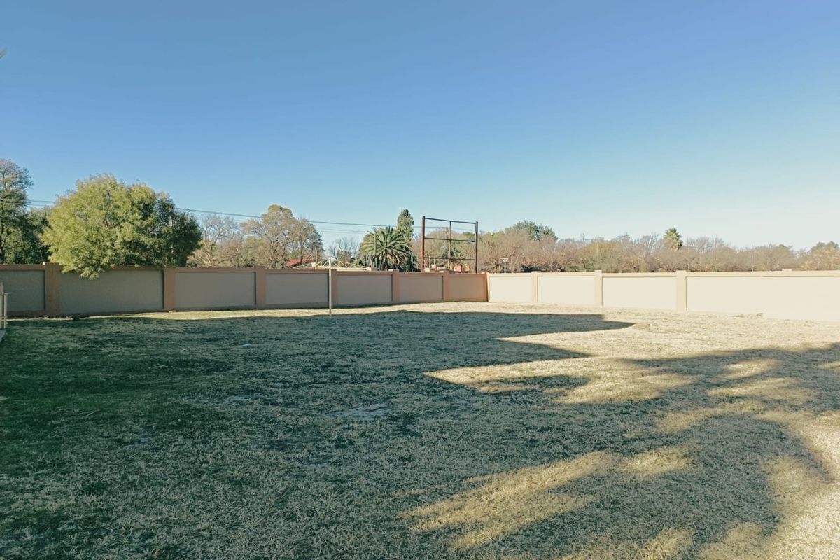 A spacious, level residential plot featuring a well-maintained perimeter wall and established grass lawn, ideal for future development.