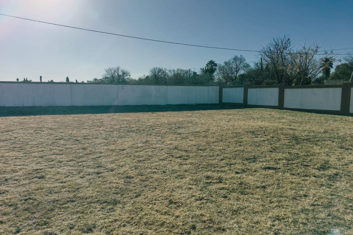 A vacant residential plot featuring a level grass area enclosed by a perimeter boundary wall.