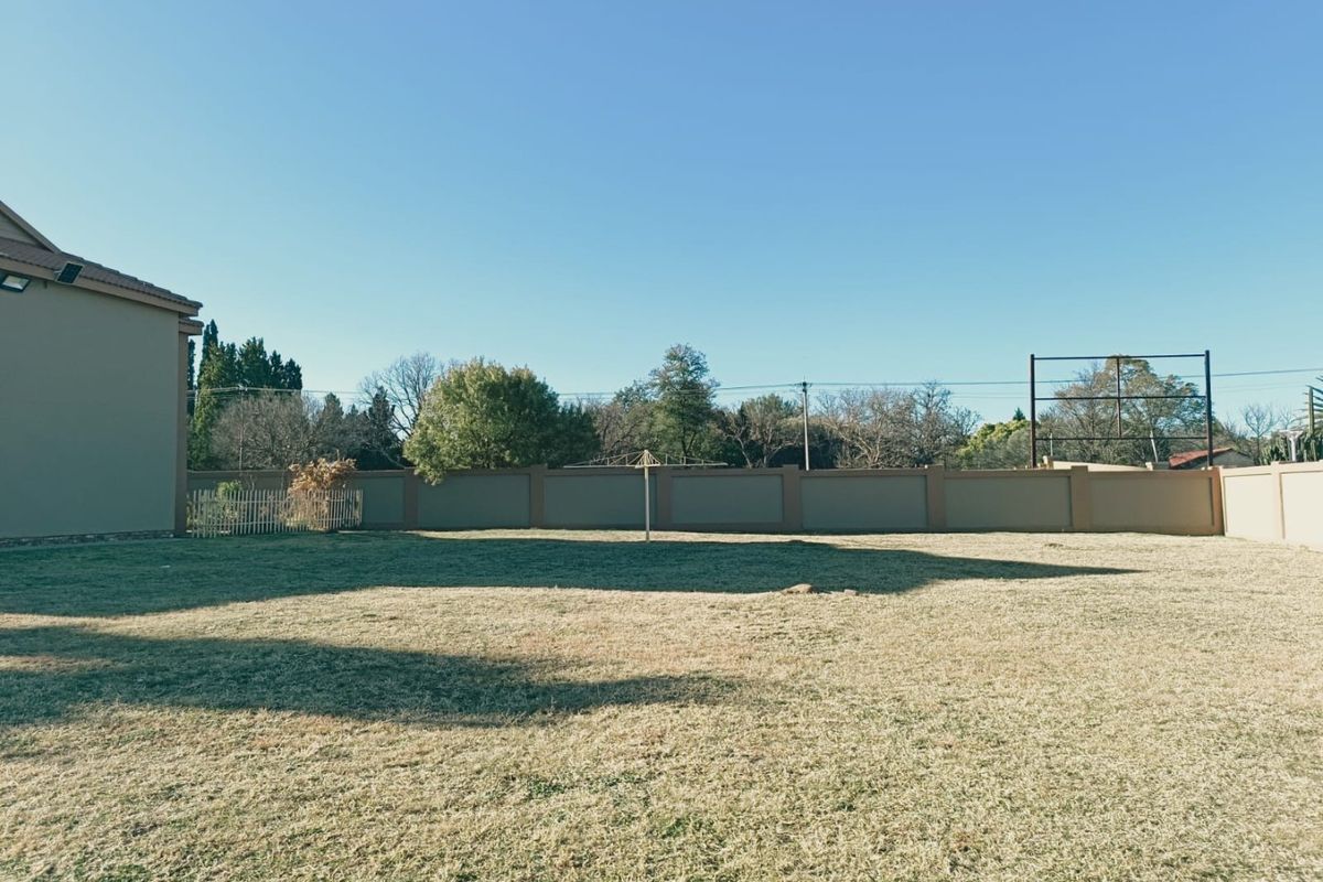 A spacious, well-maintained rear garden featuring a level lawn, perimeter boundary wall, and a rotary clothesline.