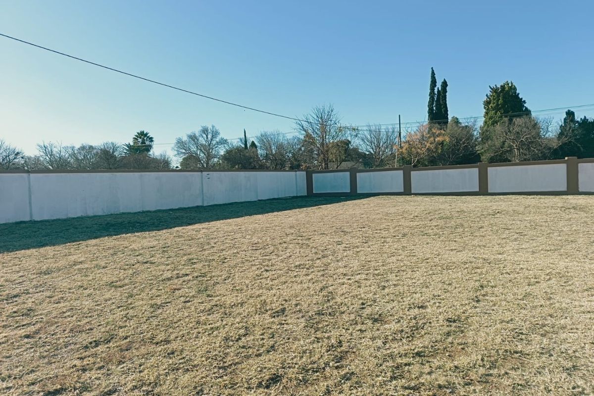 A spacious, level residential plot featuring a well-maintained grass lawn enclosed by a solid perimeter boundary wall.