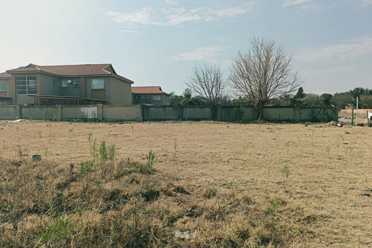 A vacant residential plot featuring dry grass and a perimeter boundary wall, offering a clear space for potential development.