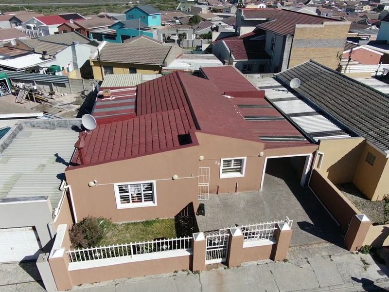 Aerial view of a residential property featuring a tiled roof, paved driveway, secure boundary wall, and an integrated garage.