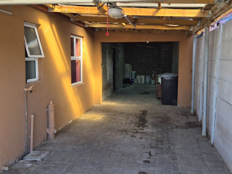 A functional outdoor garage or carport area featuring paved flooring, exposed timber roof beams, and a concrete block boundary wall.