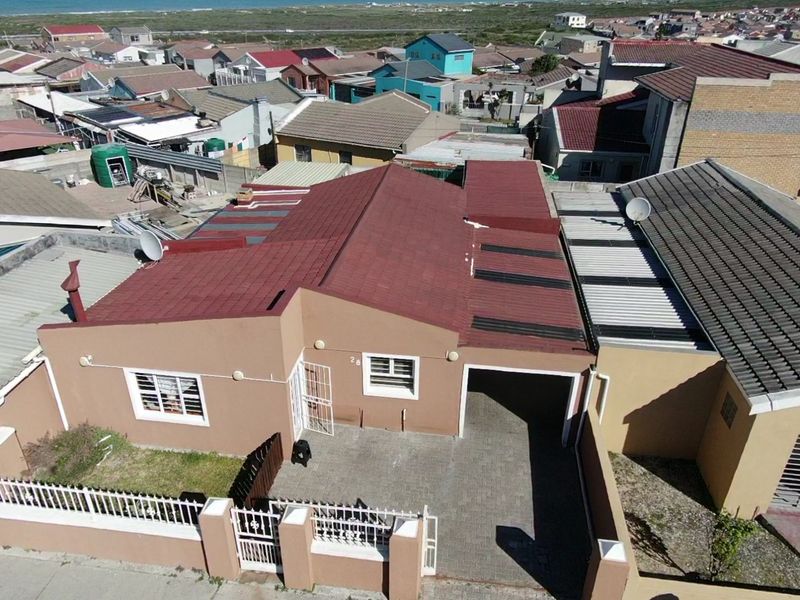 Aerial view of a residential property featuring a tiled roof, paved driveway, carport, and secure boundary walling in a suburban neighborhood.