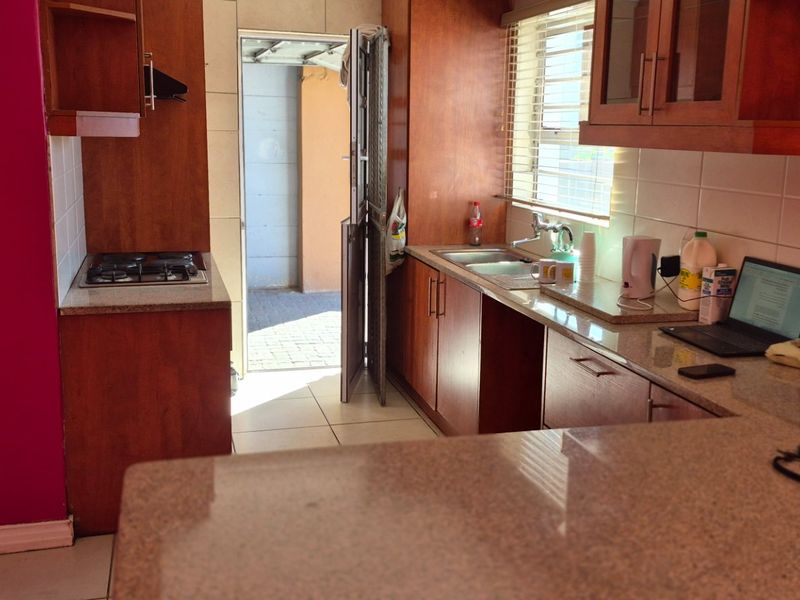 A functional kitchen featuring wooden cabinetry, granite countertops, a gas hob, and a double sink, with direct access to an outdoor area.