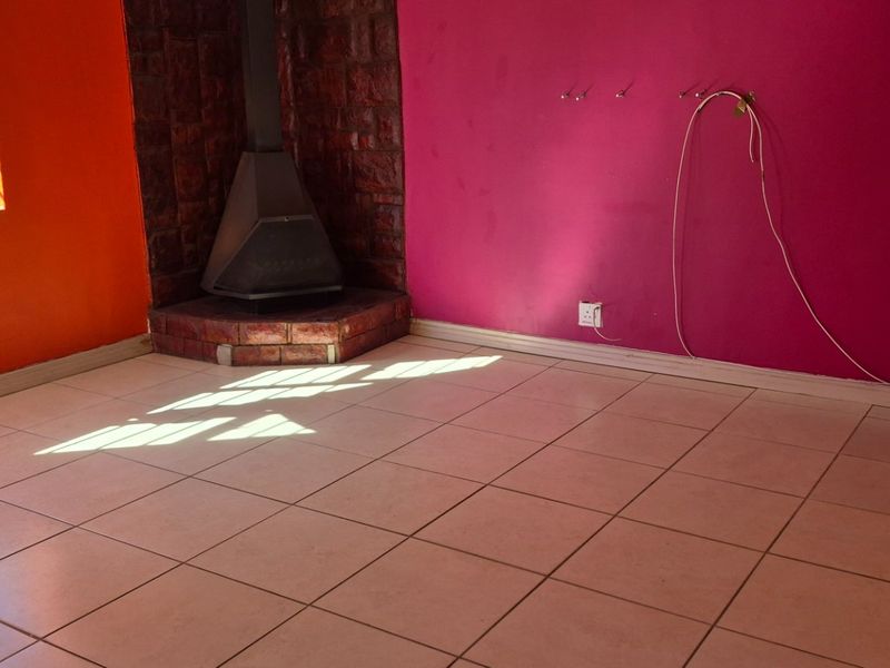 An empty living room featuring tiled flooring and a brick-surround freestanding fireplace, requiring cosmetic updates to the wall finishes.