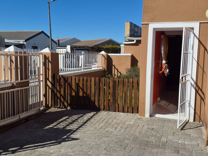A paved rear courtyard area featuring a security gate, perimeter walling with metal fencing, and a wooden gate providing access to the property exterior.
