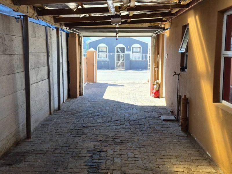 A covered outdoor parking area or garage space featuring paved flooring, a timber roof structure, and a concrete boundary wall.