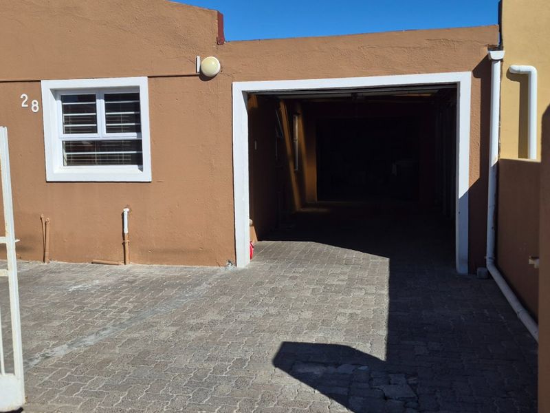 Front exterior view of the property featuring a paved driveway, integrated garage, and security gate access.
