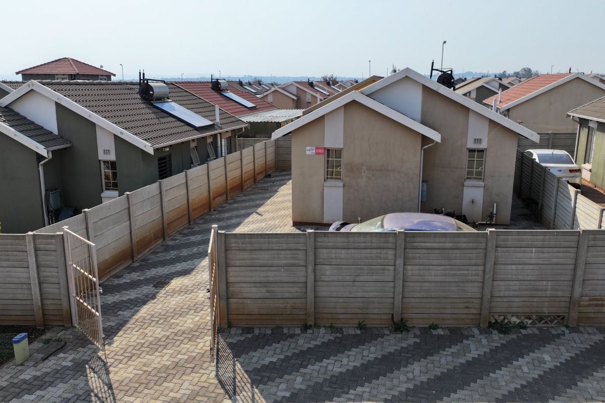 Aerial view of a residential property featuring a paved driveway, precast concrete boundary walls, and a tiled roof with a solar water heater.