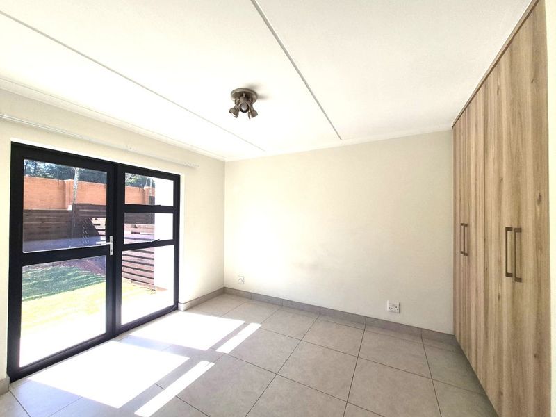 A bright, empty bedroom featuring modern tiled flooring, built-in wooden cupboards, and a glass door providing direct access to the outdoor area.