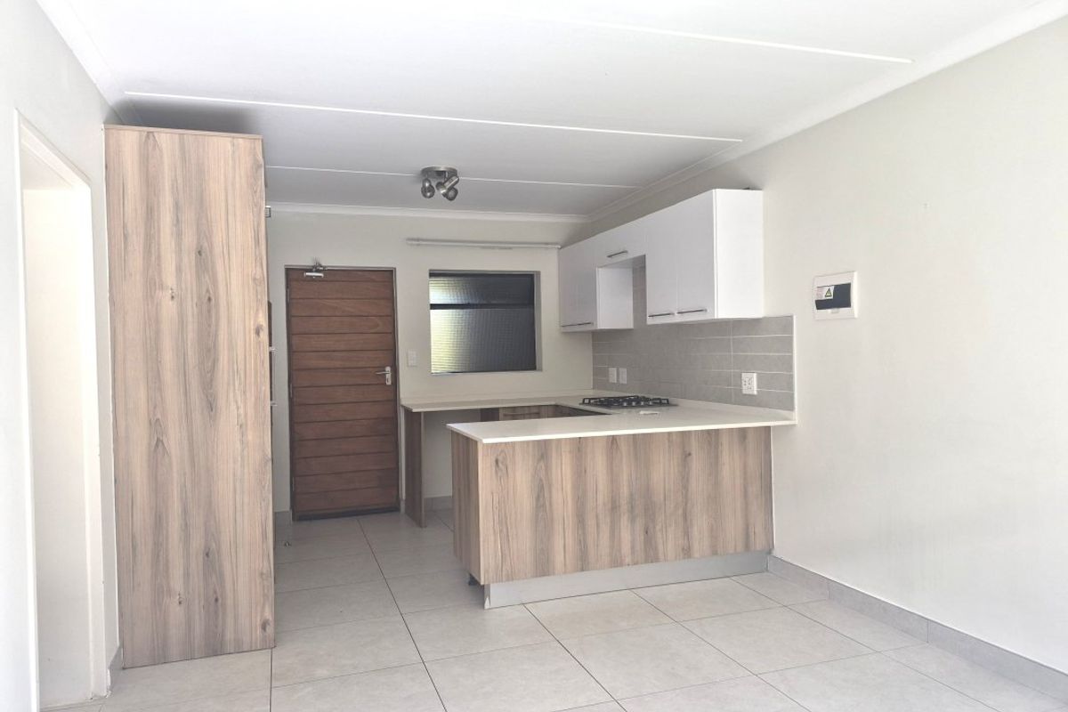 Modern open-plan kitchen featuring light wood-grain cabinetry, white stone countertops, a gas hob, and neutral tiled flooring in a clean, well-maintained space.