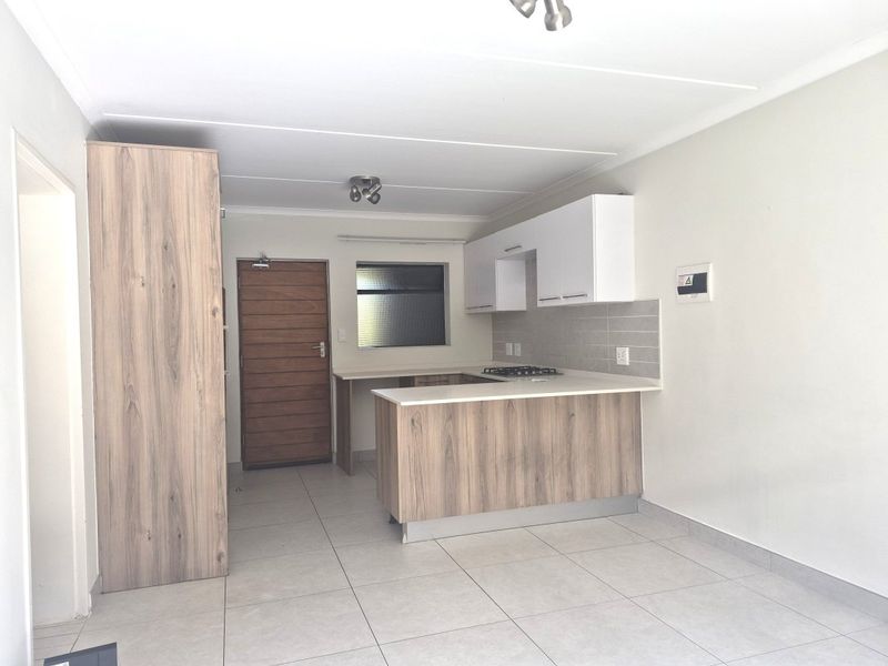 Modern open-plan kitchen featuring light wood-grain cabinetry, white stone countertops, a gas hob, and neutral tiled flooring in a clean, well-maintained space.