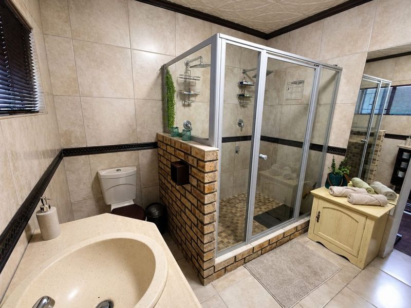 A functional bathroom featuring a built-in brick shower enclosure, tiled walls, a vanity basin, and a standard toilet.