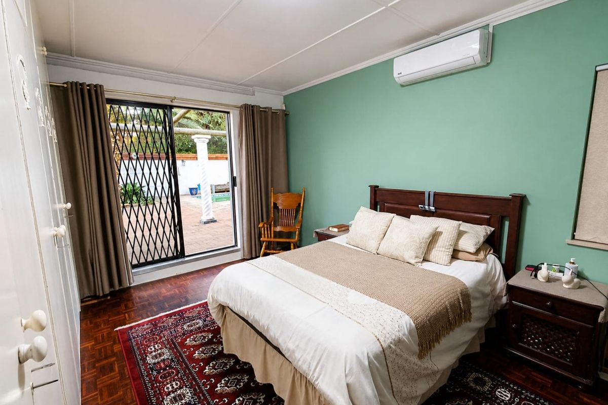 A well-maintained bedroom featuring parquet flooring, built-in cupboards, a split-system air conditioner, and a sliding door providing access to the outdoor patio area.