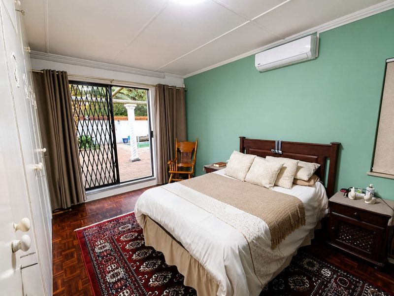 A well-maintained bedroom featuring parquet flooring, built-in cupboards, a split-system air conditioner, and a sliding door providing access to the outdoor patio area.