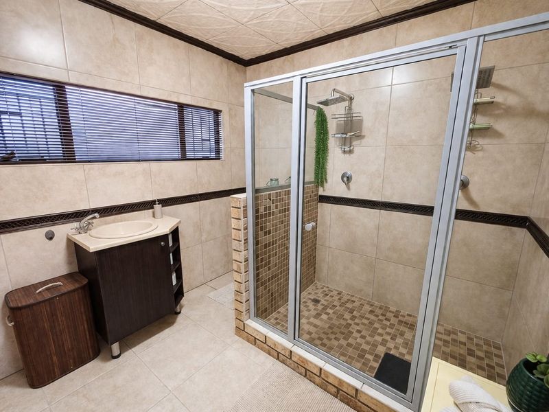 A functional bathroom featuring a walk-in shower with glass enclosure, a vanity cabinet with basin, and neutral wall and floor tiling.