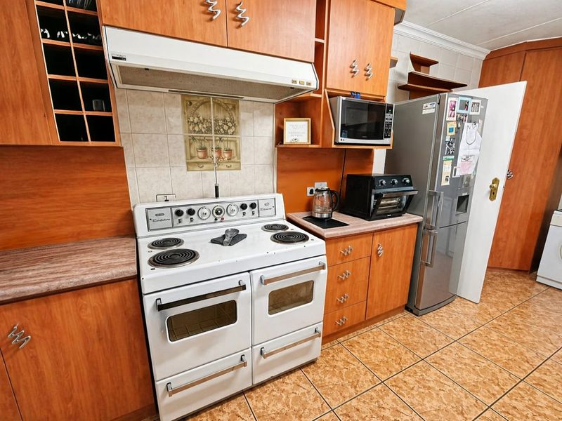 A functional kitchen featuring wood-look laminate cabinetry, ceramic tile flooring, a freestanding electric stove with extractor fan, and ample built-in storage space.