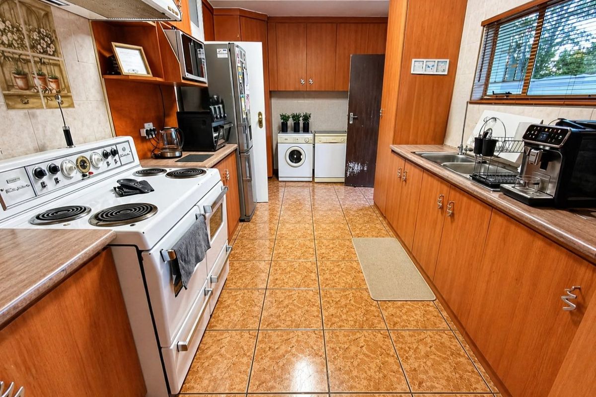 A functional kitchen featuring wood-look laminate cabinetry, tiled flooring, a freestanding electric stove, and integrated laundry space with a tiled backsplash.