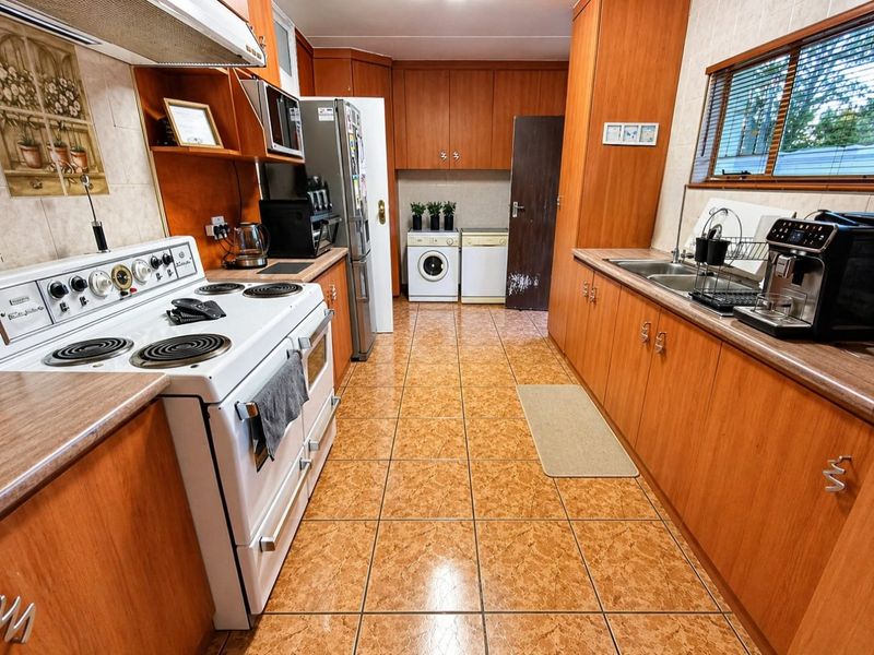 A functional kitchen featuring wood-look laminate cabinetry, tiled flooring, a freestanding electric stove, and integrated laundry space with a tiled backsplash.