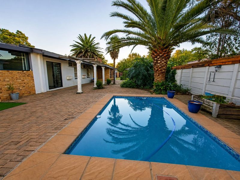A well-maintained outdoor pool area featuring a paved patio, decorative columns, and established palm trees, providing a pleasant space for relaxation and entertainment.
