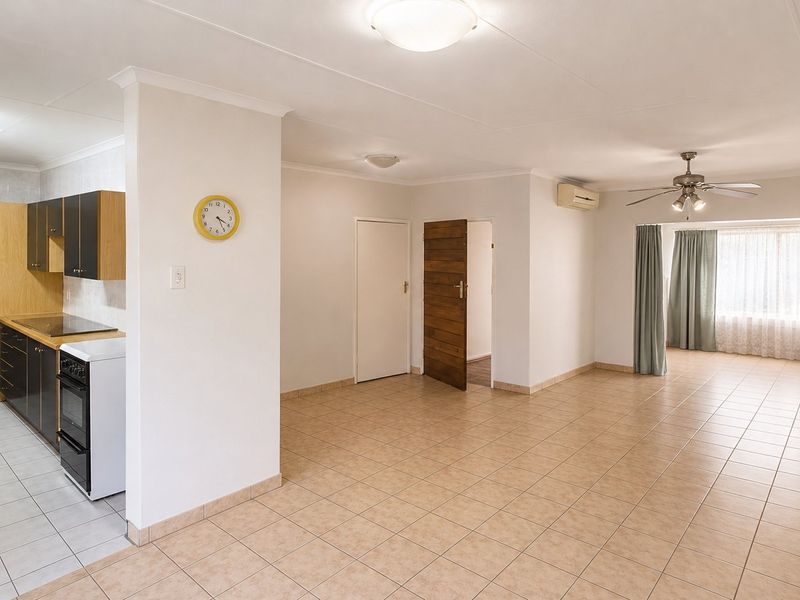 Open-plan living and kitchen area featuring tiled flooring, ceiling fan, split system air conditioning, and functional built-in kitchen cabinetry with a freestanding stove.
